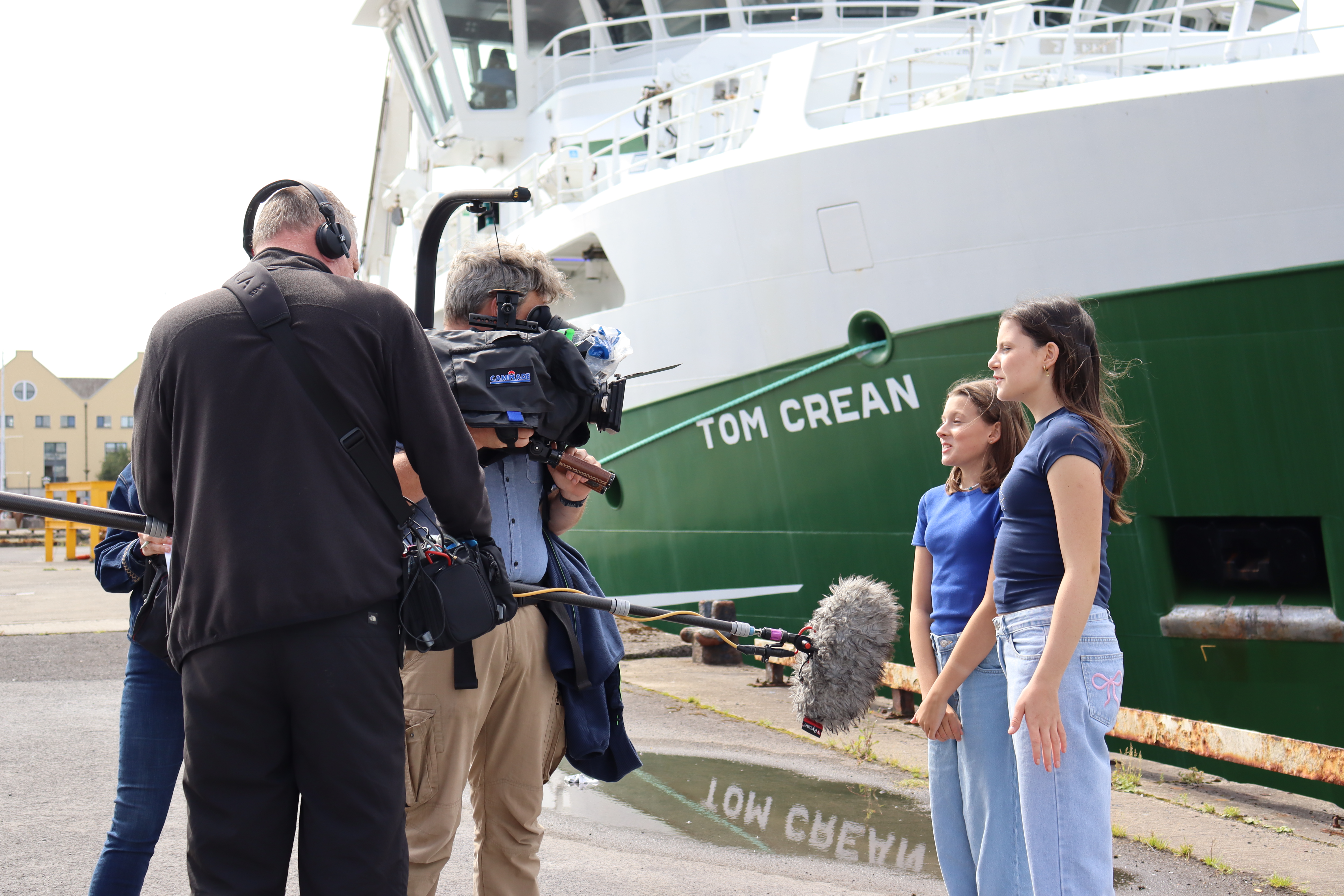 Two female school students interviewed on camera on the background of RV Tom Crean